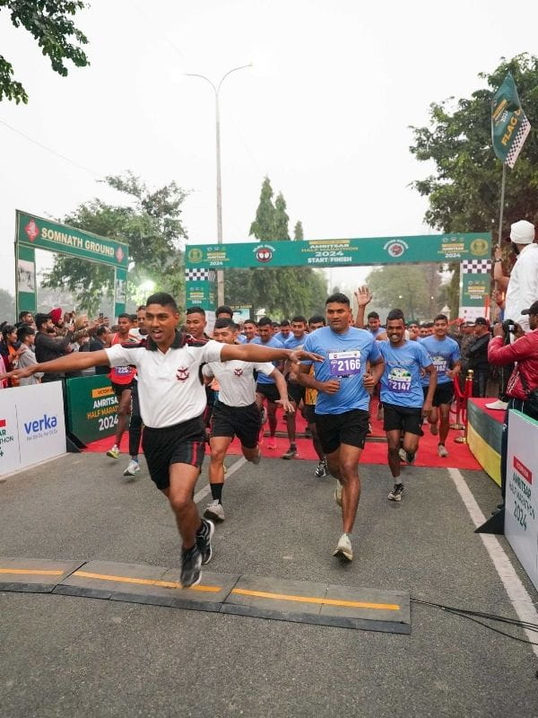 Runners sprinting from the starting line under a ceremony banner, arms outstretched as crowds cheer on both sides.
