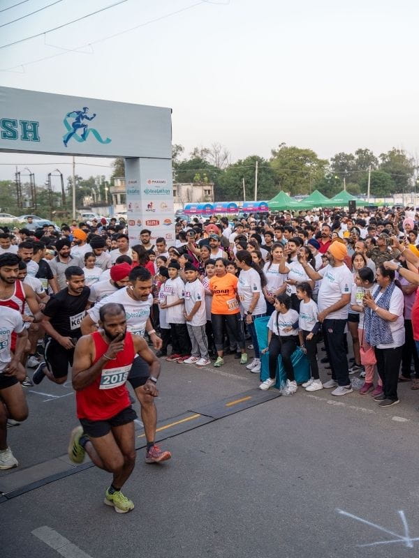 Runners sprint from the starting line as a large crowd of spectators watches at a road race event.